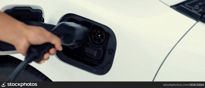 Closeup focus hand insert EV charger plug to electric vehicle from charging station. Progressive alternative clean energy engine car technology. Renewable EV car for eco-friendly transportation idea.. Closeup focus hand insert EV charger to progressive electric rechargeable car.