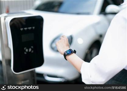 Closeup focus progressive wearable watch show electric car battery status that being recharge at charging station point in the city. Digital interface, data from EV car display on smartwatch.. Closeup progressive watch focus show EV car battery status recharging.