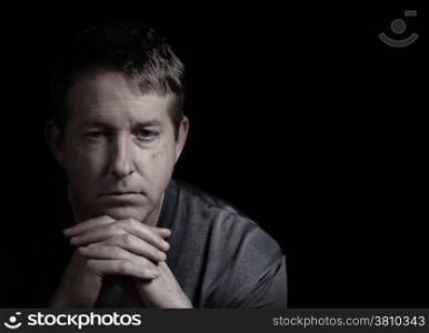Closeup front view of mature man, looking forward, with chin resting in folded hands on dark background