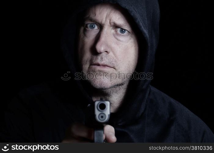 Closeup front view of mature man, looking forward, with gun in hand on black background