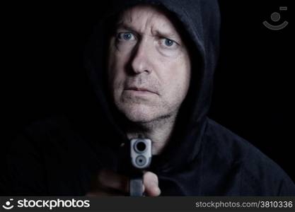 Closeup front view of mature man, looking forward, with gun in hand on black background