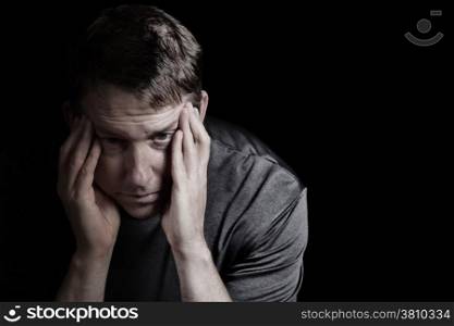 Closeup front view of mature man with head down, touching his temples, while displaying depression on black background