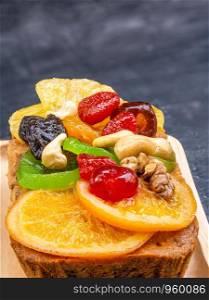Closeup fruitcake pasted with sweetend fruits in wooden plate on black wooden background.