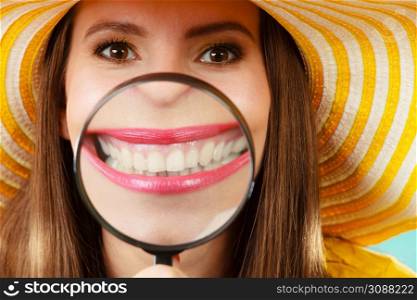 Closeup funny woman in summer hat smiling and show teeth through a magnifying glass