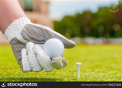 closeup hand holding a golf ball near the tee