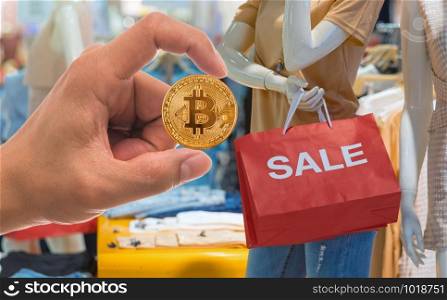 Closeup hand holding bitcoin mockup over Part of female mannequin dressed in casual clothes holding the Sales paper shopping bag in the shopping department store, Business and future shopping concept