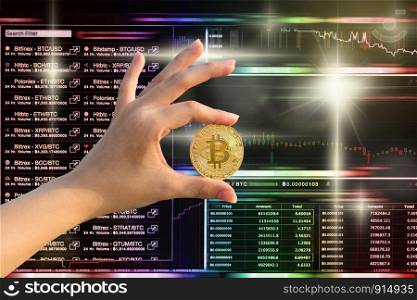 Closeup hand holding bitcoin over the Cryptocurrency trading screen, Bitcoin exchange screen of trading information, Block chain technology of Crypto concept, Business and market trade concept