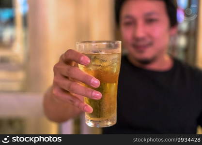 Closeup hand holding glass of beer from Asian young man in happiness action in pub and restaurant with low light place, relax and drink concept