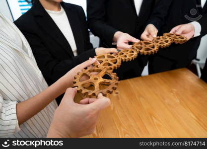 Closeup hand holding wooden gear by businesspeople wearing suit for harmony synergy in office workplace concept. Group of people hand making chain of gears into collective form for unity symbol.. Group of people making chain of gears into collective form for harmony symbol.