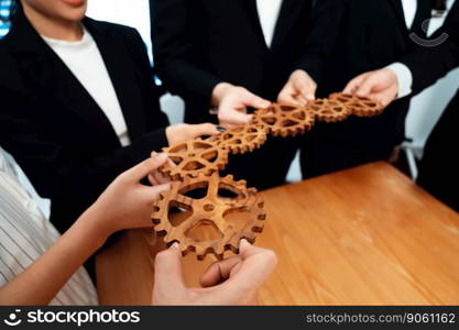 Closeup hand holding wooden gear by businesspeople wearing suit for harmony synergy in office workplace concept. Group of people hand making chain of gears into collective form for unity symbol.. Group of people making chain of gears into collective form for harmony symbol.