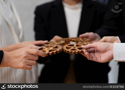 Closeup hand holding wooden gear by businesspeople wearing suit for harmony synergy in office workplace concept. Group of people hand making chain of gears into collective form for unity symbol.