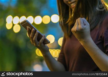 Closeup hand of Asian woman using smartphone and celebrating at outdoor park, Business and Lifestyle concept