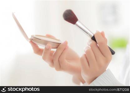 Closeup hand of beauty young asian woman with face looking mirror applying makeup with brush cheek in the bedroom, beautiful girl holding blusher facial, skin care and cosmetic concept.