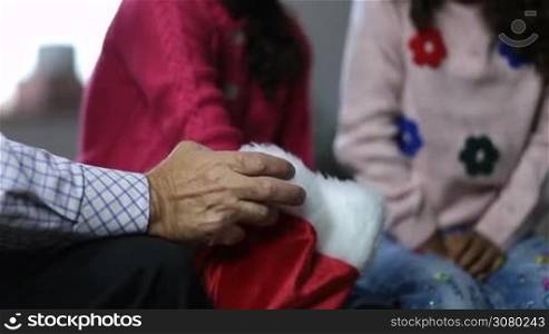 Closeup hand of grandfather holding santa hat and children choosing piece of paper with names from it as cheerful family playing secret santa christmas game. Diverse family spending leisure and having fun on winter holidays.
