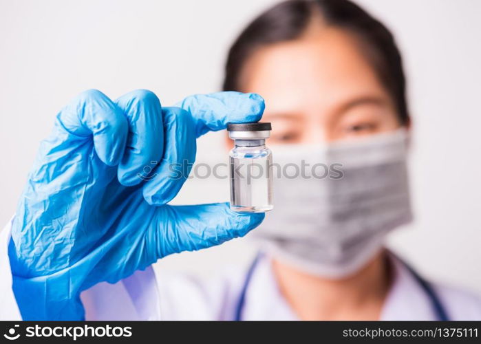 Closeup hand of woman doctor or scientist in doctor&rsquo;s uniform wearing face mask protective in lab holding medicine liquid vaccines vial bottle, coronavirus or COVID-19 concept, studio shot isolated