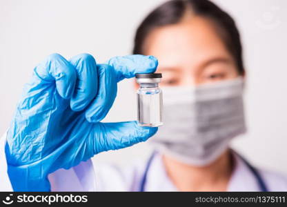 Closeup hand of woman doctor or scientist in doctor&rsquo;s uniform wearing face mask protective in lab holding medicine liquid vaccines vial bottle, coronavirus or COVID-19 concept, studio shot isolated
