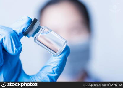 Closeup hand of woman doctor or scientist in doctor&rsquo;s uniform wearing face mask protective in lab holding medicine liquid vaccines vial bottle, coronavirus or COVID-19 concept, studio shot isolated