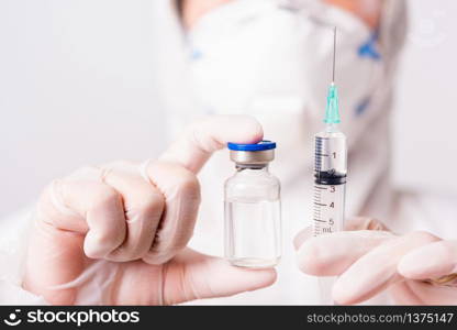 Closeup hand of woman doctor or scientist in PPE suite uniform wearing face mask protective in lab hold medicine liquid vaccine vial bottle and syringe, coronavirus or COVID-19 concept white isolated