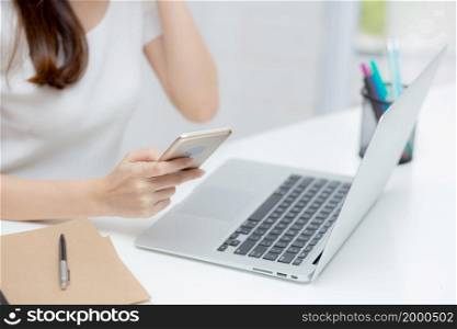 Closeup hand of young woman working laptop computer and reading smartphone on internet online on desk at home, freelance girl using phone with social media, business and communication concept.