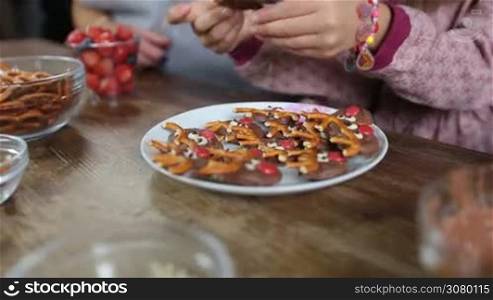 Closeup hands of multi generation family hands taking xmas decorated homemade cookies from plate over rustic wooden table background. Grandmother, daughter and grandaughter eating tasty chocolate cookies in the kitchen.180 degree dolly shot.
