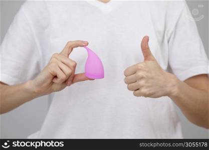 closeup hands of woman holding menstrual cup on white t-shirt background showing thumb up, having period, dislike to use napkins or tampons. selective focus