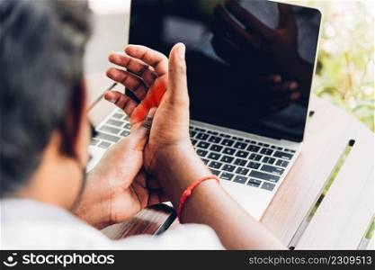 Closeup hands the Asian black man holding his wrist pain from using laptop computer he working long time, Injury office syndrome hand pain by occupational disease concept