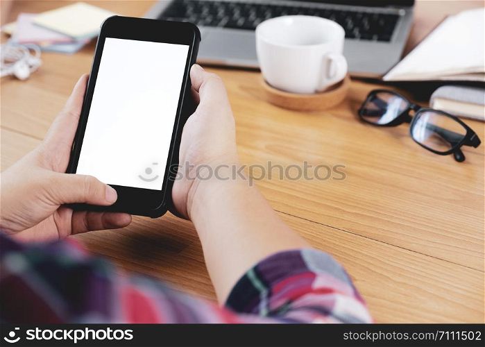 Closeup hands using smartphone mockup at the office desk. Blank screen mobile phone for graphic display montage.