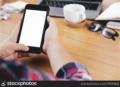 Closeup hands using smartphone mockup at the office desk. Blank screen mobile phone for graphic display montage.