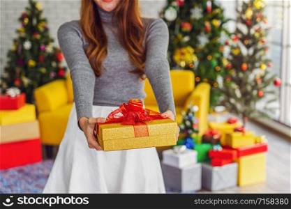 Closeup happiness asian woman wearing colorful red sweaters with hat holding and giving the gift box to other for merry christmas celebration, asian or asean indoors party, xmas and new year concept