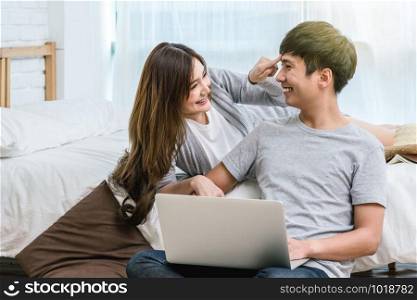 Closeup Happy Asian Lover or couple talking and smiling when using technology laptop on the bed in bed room at modern home, young women pointing to the forehead of boyfriend, Lover and life style concept,