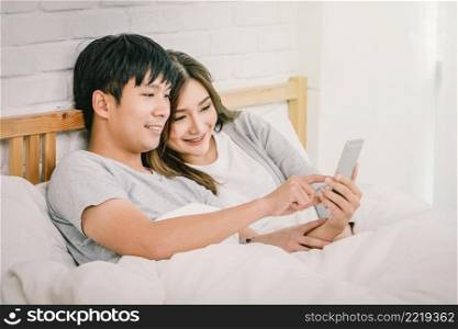 Closeup Happy Asian Lover or couple using technology smart phone on the bed in bed room at modern home, boyfriend pointing to the mobile phone, Lover and life style concept,