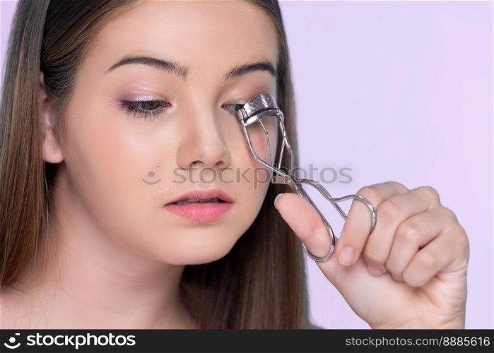 Closeup happy young charming bru≠tte holding eyelash cur≤r in her hand as makeup accessory. Beautiful girl applying eyelash cur≤r in studio with isolated background for©space.. Closeup happy young charming bru≠tte holding eyelash cur≤r in her hand.