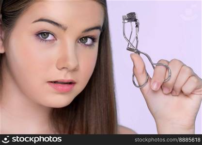 Closeup happy young charming brunette holding eyelash curler in her hand as makeup accessory. Beautiful girl applying eyelash curler in studio with isolated background for copyspace.. Closeup happy young charming brunette holding eyelash curler in her hand.