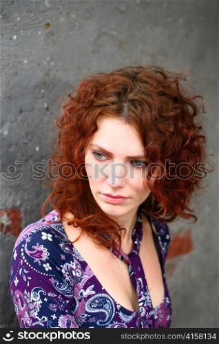 closeup headshot portrait of an attractive young redhead woman beside a brick wall