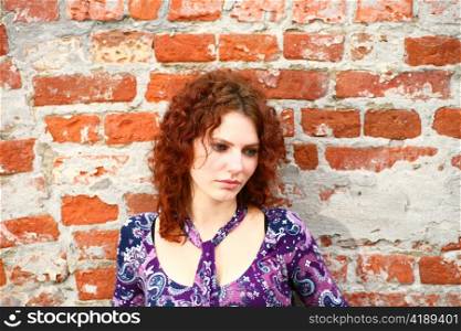 closeup headshot portrait of an attractive young redhead woman beside a brick wall