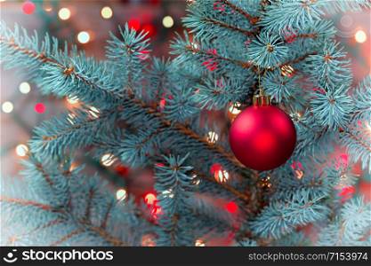 Closeup horizontal image of a single red Christmas ornament hanging from real pine tree branch with glowing lights in vintage format