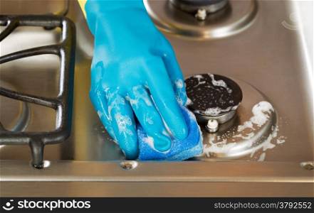 Closeup horizontal image of hand wearing rubber glove while cleaning stove top range with soapy sponge