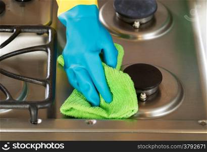 Closeup horizontal image of hand wearing rubber glove while cleaning stove top range with microfiber rag