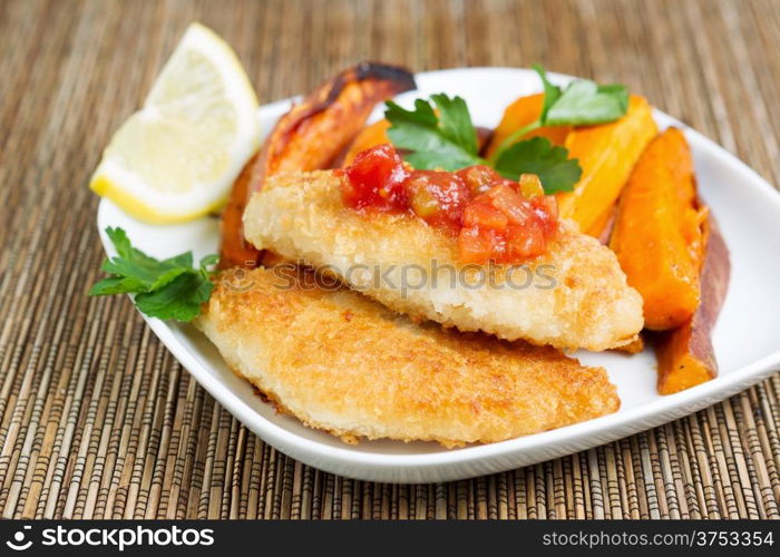Closeup horizontal of golden crisp fried cod fish with salsa sauce on top with Yam Fries in background