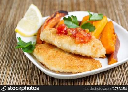 Closeup horizontal of golden crisp fried cod fish with salsa sauce on top with Yam Fries in background