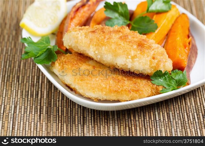 Closeup horizontal of golden crisp fried fish and yams in white plate with bamboo place mat underneath
