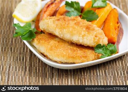 Closeup horizontal of golden crisp fried fish and yams in white plate with bamboo place mat underneath
