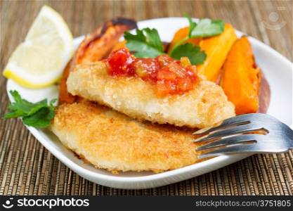 Closeup horizontal of golden crisp fried fish with salsa sauce on top and Yam Fries on side