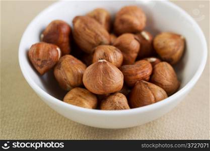 Closeup horizontal photo of a bowl filled with raw whole nuts lying on top of a textured table cloth