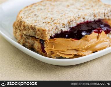 Closeup horizontal photo of a peanut butter and jelly sandwich cut in half, inside white plate on textured table cloth underneath