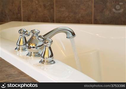 Closeup horizontal photo of chrome faucet running water into soaking tub in master bathroom