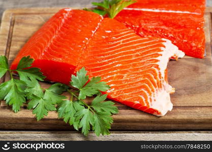 Closeup horizontal photo of fresh red salmon fillets on traditional wooden server with parsley on the side and rustic wood underneath