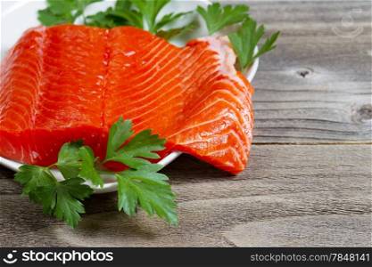 Closeup horizontal photo of fresh sockeye salmon fillet, partially out of plate, with parsley on the side and rustic wood underneath