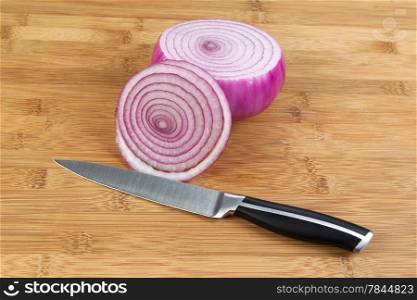 Closeup horizontal photo of freshly sliced red onion with kitchen knife in front and natural bamboo wood underneath