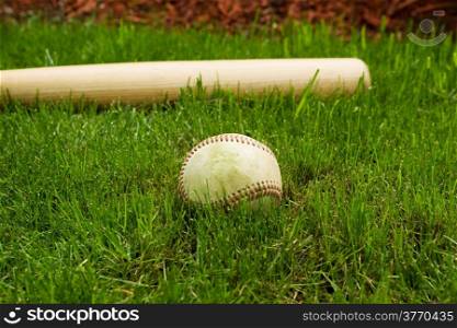 Closeup horizontal photo of old baseball in front of wooden bat on natural grass field